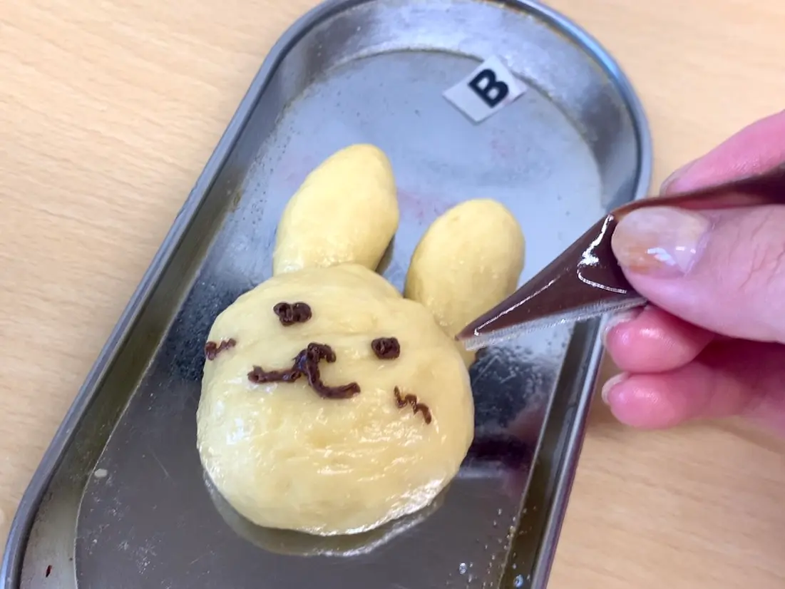 最後にチョコペンで顔を入れたら完成！焼き上がるのを待ちながら、次の体験！